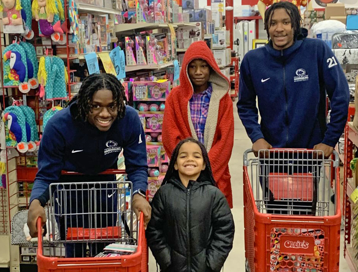 isaiah milien and malik holland pose with a local child at the 2022 shop with a cop holiday event